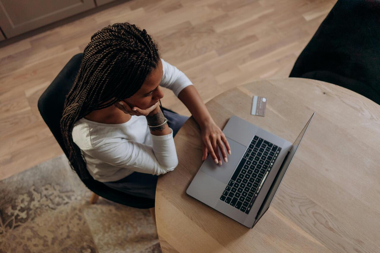 Mulher sentada na cozinha usando um notebook sobre a bancada, com expressão séria enquanto trabalha.
