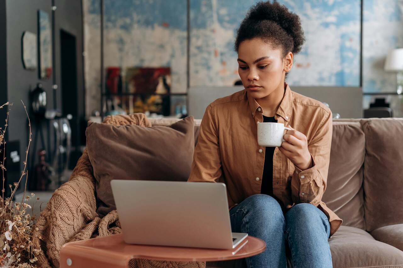 Pessoa sentada em ambiente acolhedor com laptop e caf&eacute;, pesquisando qual a melhor operadora de internet residencial para garantir conectividade est&aacute;vel e eficiente durante atividades de trabalho ou estudo remoto. 