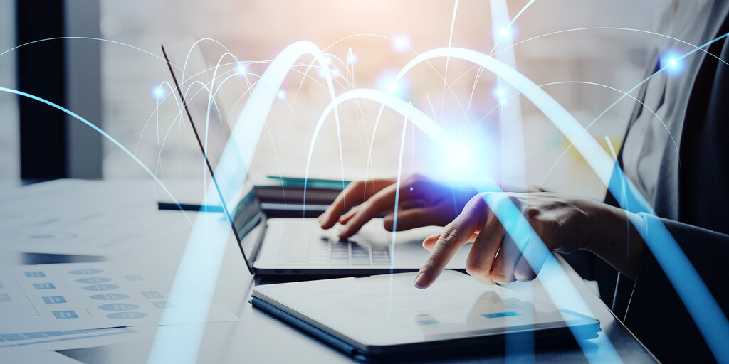 Pessoa utilizando notebook e tablet com efeitos de conexão digital, ilustrando tráfego de dados e vantagens do link dedicado.