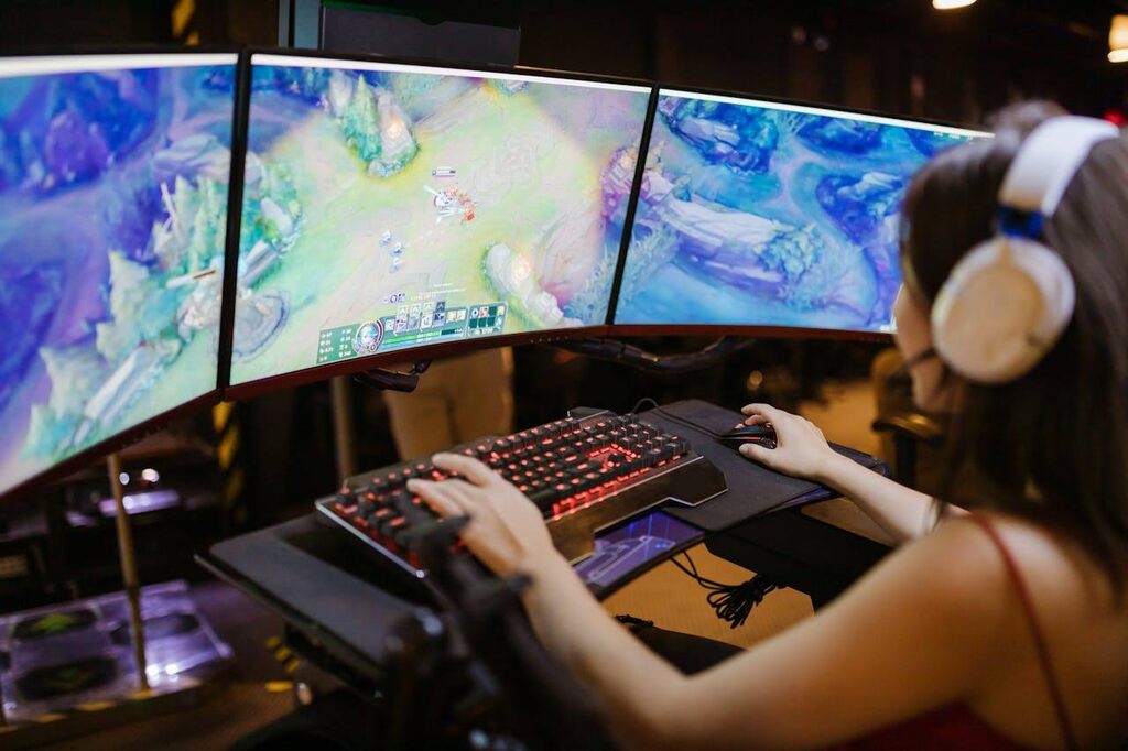 pessoa jogando online em computador de 3 telas, representando a conexão via internet a cabo ou fibra