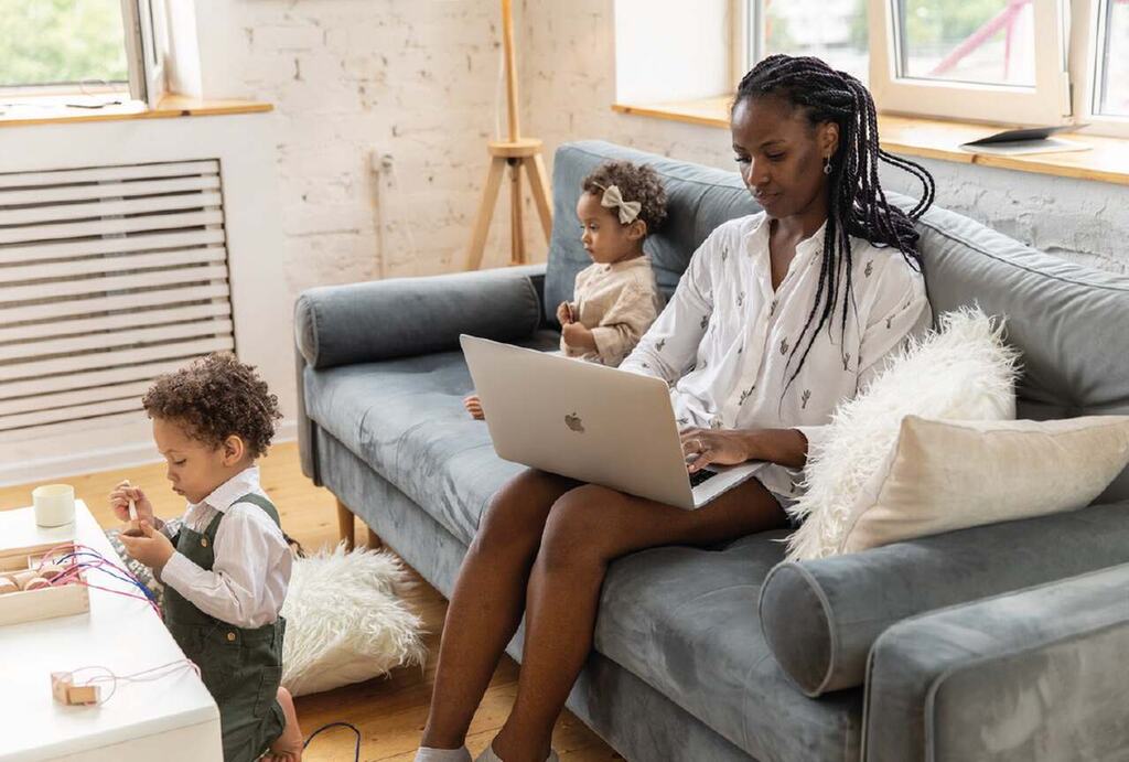 mulher em casa no sofá acessando internet mega e giga pelo notebook, ao lado de duas crianças