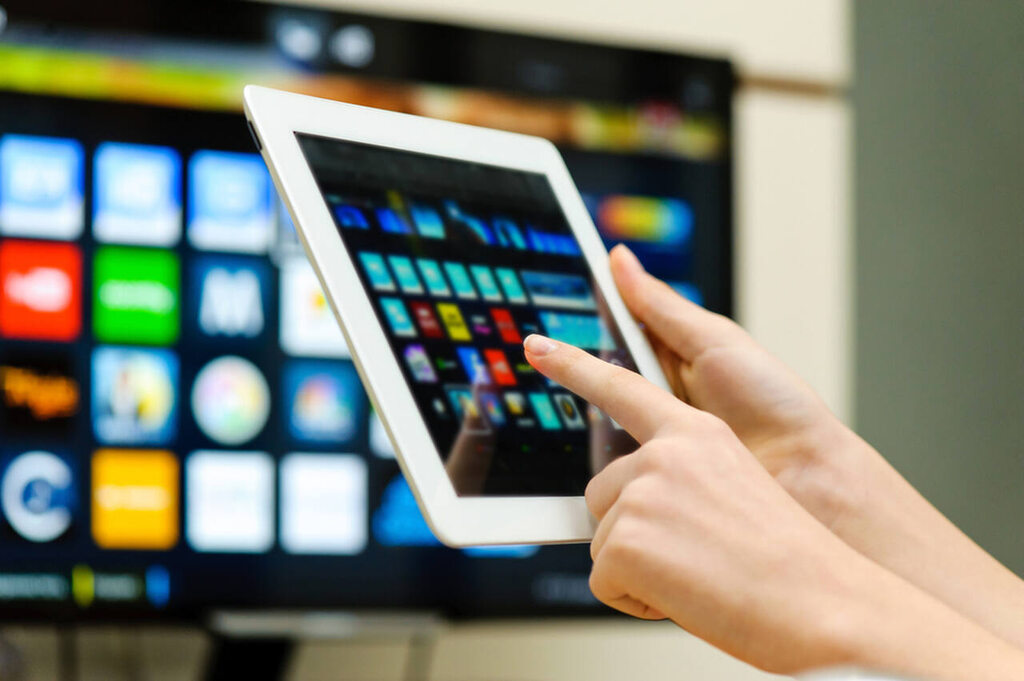 pessoa com tablet em frente à televisão, aprendendo como conectar a TV na internet