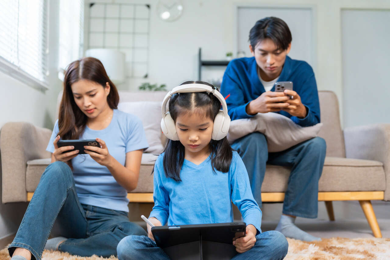 Família utilizando vários dispositivos conectados à internet em casa, como notebook, tablet e celular ao mesmo tempo