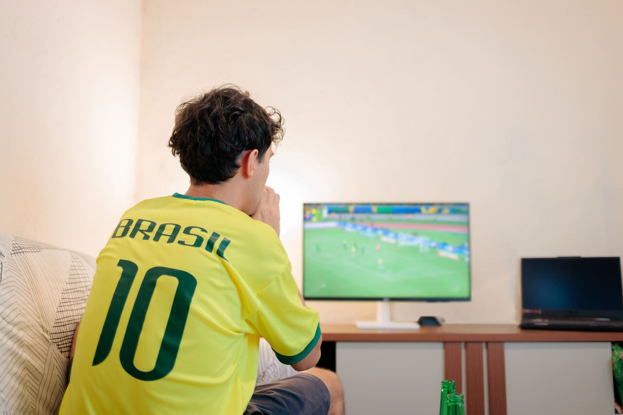 Pessoa assistindo futebol na TV, demonstrando uso de largura de banda para transmissão de vídeo online