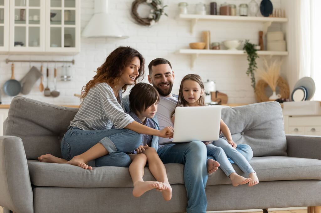 Fam&iacute;lia usando notebook no sof&aacute; em casa confort&aacute;vel, simbolizando conex&atilde;o de internet est&aacute;vel para v&aacute;rios dispositivos.