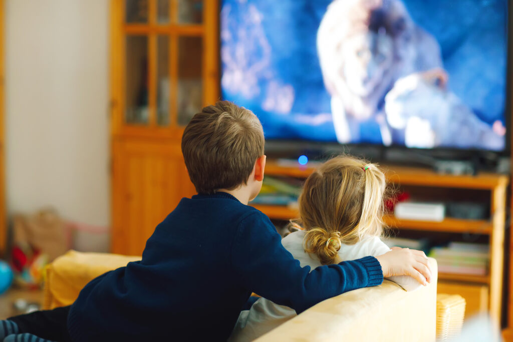 Duas crian&ccedil;as sentadas no sof&aacute; da sala assistindo a um document&aacute;rio sobre vida selvagem e natureza na televis&atilde;o.