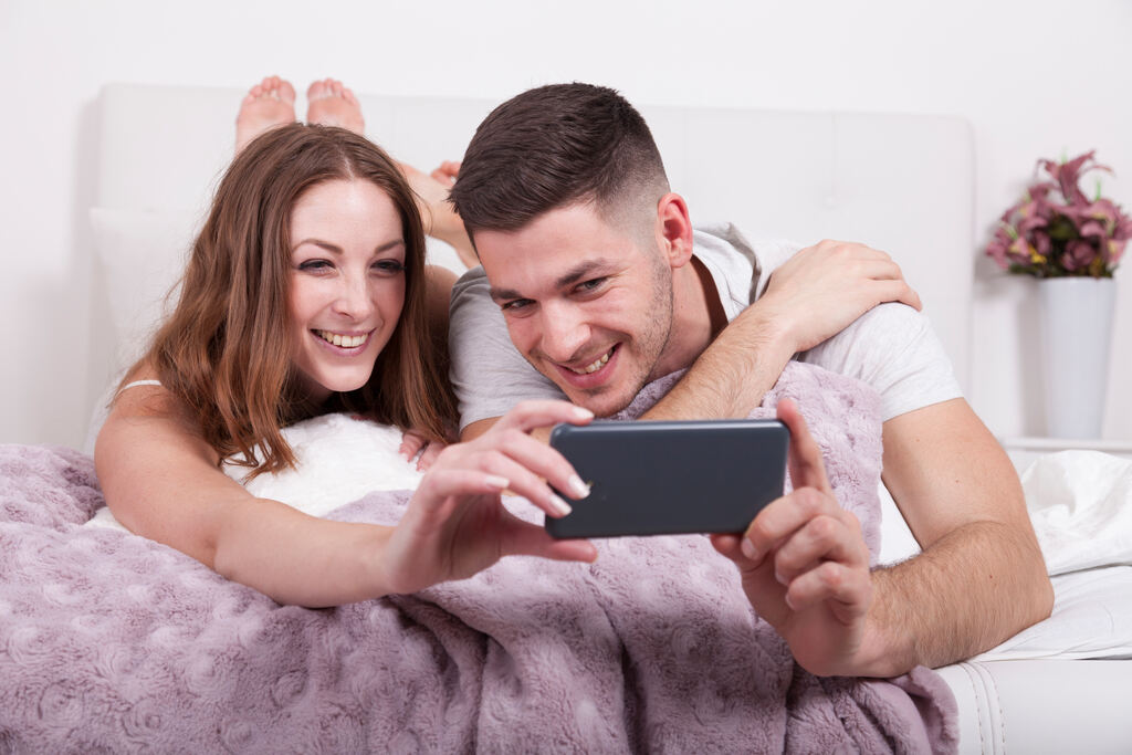 Casal usando celular na cama, representando o que fazer quando o Wi-Fi n&atilde;o chega no quarto