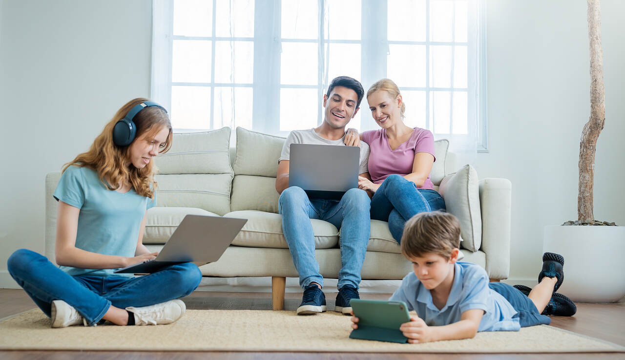 Família usando internet residencial em múltiplos dispositivos, incluindo smartphone, tablet e fones de ouvido em casa